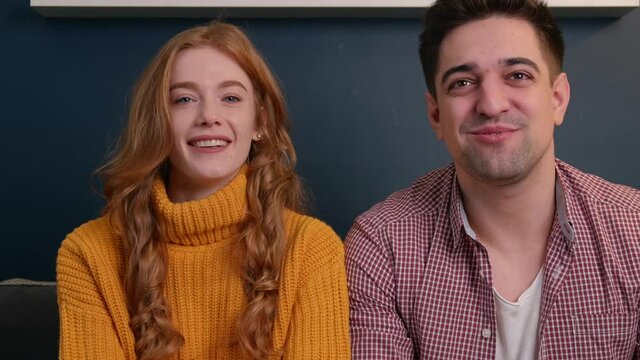 Close up video of a caucasian couple discussing at camera with somebody smiling and cheering on the couch