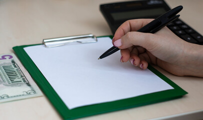 Women's hand writes on a white sheet against the background of calculator and banknotes