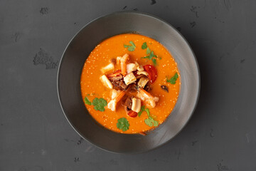 Tom yam Thai soup in black bowl served on gray background