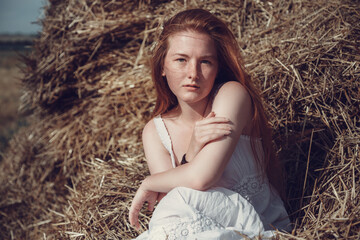 Young ginger woman in the wheat field looking relaxed.