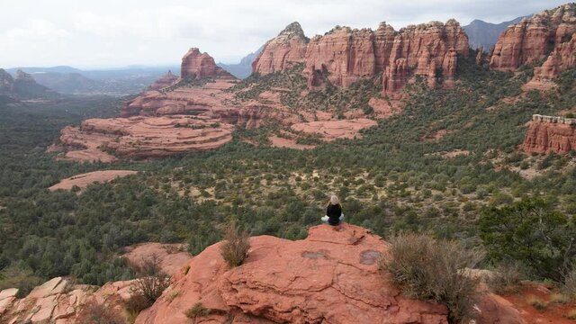 Woman meditating on the edge of mountain, Red Rocks, Sedona, Arizona. Aerial forward