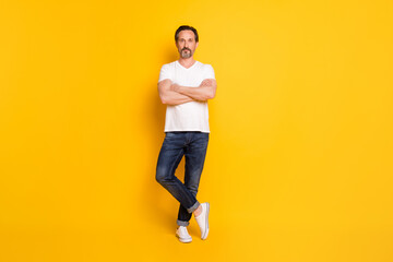 Fototapeta na wymiar Photo of self-assured cool bearded man posing folded arms wear white t-shirt jeans footwear isolated yellow background