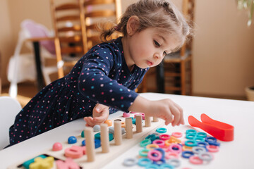 Little girl play in educational game for children. Wooden game with different colors and numbers. Intecactive game for clever kids. Girl spent time at home during quarantine - obrazy, fototapety, plakaty