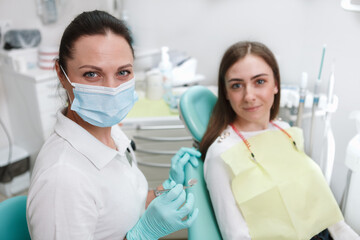 Female dentist wearing protective face mask, looking to the camera while working with patient