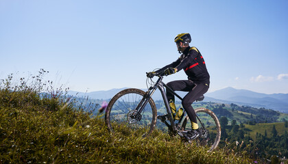 Fototapeta na wymiar Joyful male cyclist riding bicycle uphill under blue sky.