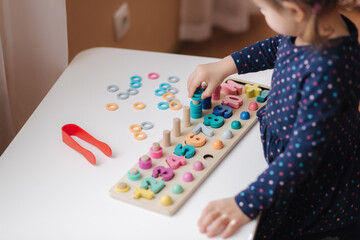 Closeup of kid's hand putting color rings on wooden column. Little girl play in educational game for children at the table. Wooden game with different colors and numbers. Intecactive game for clever