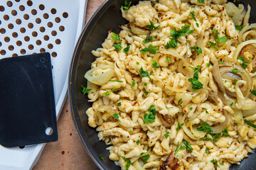 Spaetzle or Spätzle egg noodle pasta with onions, parsley and seasoning in a pan. Traditional European cuisine dish (Swabian, German, Austrian). Handmade gluten free Knöpfle. Grater in background