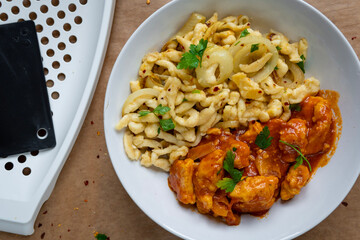 Spaetzle or Spätzle egg noodle pasta with chicken, onions and seasoning. Traditional European cuisine dish (Swabian, German, Austrian, Hungarian). Gluten free Knöpfle bowl with a grater in background.