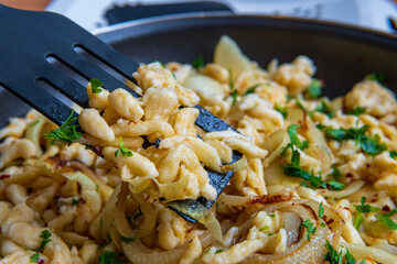 Spatula taking spaetzle or Spätzle egg noodle pasta with onions and seasoning from a pan. Traditional European cuisine dish (Swabian, German, Austrian, Hungarian). Handmade, tasty, gluten free Knöpfle