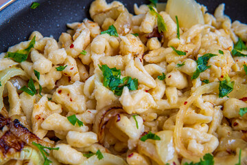 Closeup on spaetzle or Spätzle egg noodle pasta with onions, parsley and seasoning in a pan. Traditional European cuisine dish (Swabian, German, Austrian). Handmade, tasty, gluten free Knöpfle, served