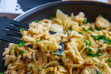 Spatula taking spaetzle or Spätzle egg noodle pasta with onions and seasoning from a pan. Traditional European cuisine dish (Swabian, German, Austrian, Hungarian). Handmade, tasty, gluten free Knöpfle