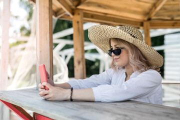 pretty lady holding cell and doing selfie near wooden gazebo at hot summer day