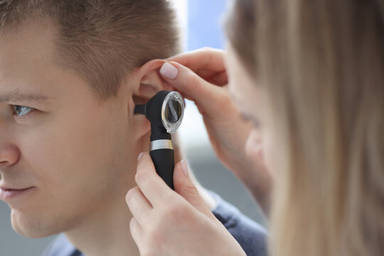 Doctor holding otoscope in his hand in front of patient ear closeup