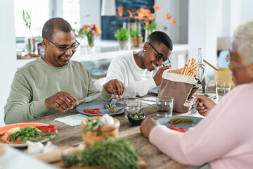 Fototapeta na wymiar Happy afro Latin family eating healthy lunch with fresh vegetables at home - Food and parents unity concept