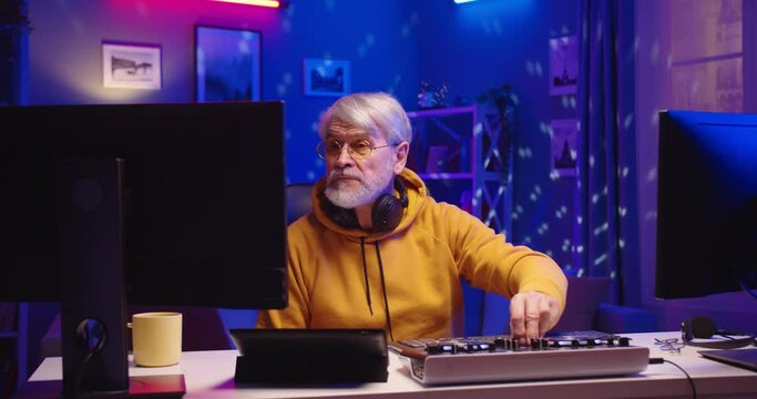 Portrait of Caucasian old man DJ playing music at home recording studio workshop. Senior male making music on equipment in room, creative atmosphere music. Sound beat maker. Colorful Neon light