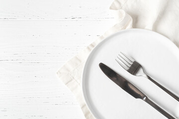 An empty plate and cutlery on a white wooden table. Top view.