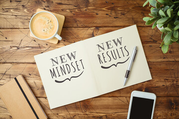 New mindset and new results text on notebook on wooden table with coffee cup and smartphone...