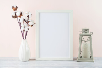 Blank picture frame mockup with cotton branch and lantern on white wooden table. Home office concept. Scandinavian interior design