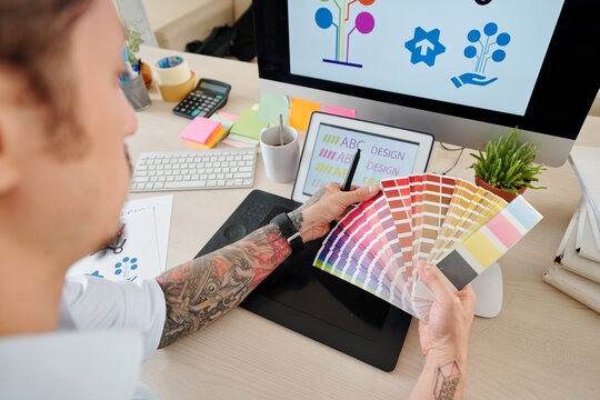 Hands of graphic designer looking at palette and choosing color for company logog