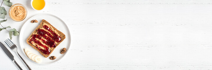 Homemade peanut butter sandwich with raspberry jam and banana on white wooden background. Top view.