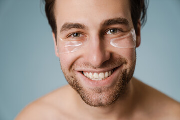 Shirtless white man with under eye patches smiling at camera