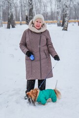 Portrait of an elderly woman with a dog. Woman with pekingese dog walking on the snowy field.