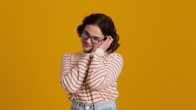 A pleased young teenager girl in eyeglasses is feeling good and looking at something cute standing isolated over yellow background in studio