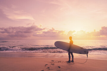 Man hold surfboard standing at tropical sunset beach background. Summer vacation and sport adventrue concept. © tonktiti
