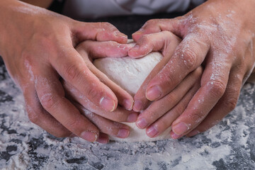 Mother and daughter's hands form hearts in dough.