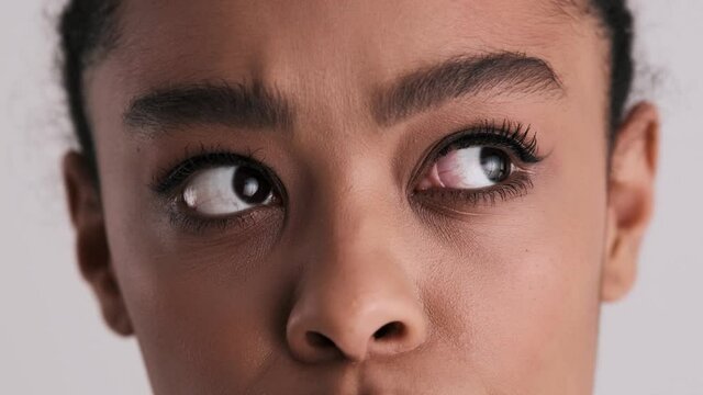 A close-up cropped view of a thinking woman is moving her eyes around isolated over a gray background in the studio