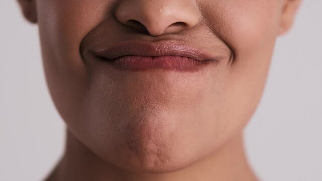 A close-up cropped view of a young woman is licking her teeth isolated over a gray background in the studio