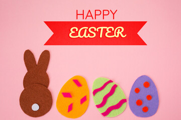 Easter holiday concept. Cut out of felt applications of colourful eggs and brown rabbit. Pink background. Flat lay. Copy space
