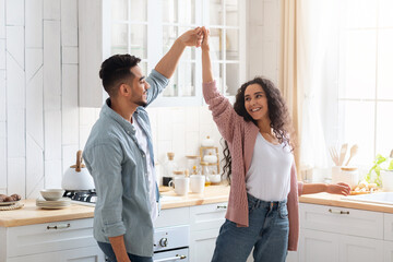 Happy Middle Eastern Couple Dancing Together In Kitchen, Having Fun At Home