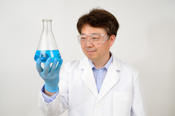 Portrait of a middle-year Asian male scientist wearing a white lab gown and gloves and holding an...