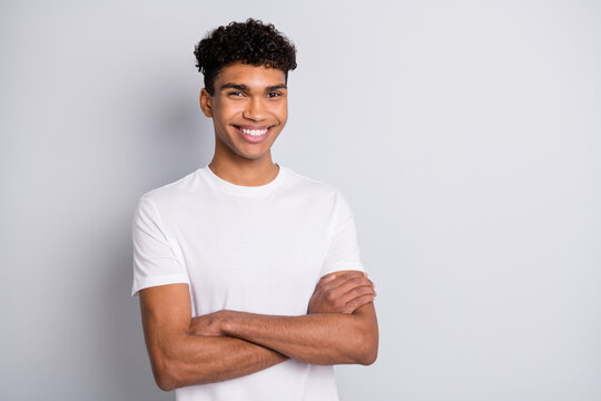 Photo of brunet optimistic curly guy stand arms crossed wear white t-shirt isolated on grey color background