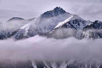 Majesty of nature concept: covered with snow after a recent snowfall rocky peak rises above the clouds at sunrise