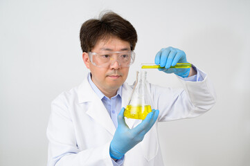 Portrait of a middle-year Asian male scientist wearing a white lab gown and gloves and holding an...