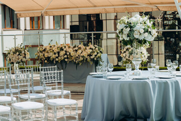 Wedding table setting decorated with fresh flowers in a brass vase. Wedding floristry. Banquet table for guests outdoors with a view of green nature. Bouquet with roses, eustoma and eucalyptus leaves.