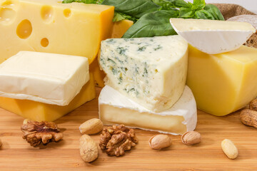 Different types cheese among greens and nuts on wooden surface