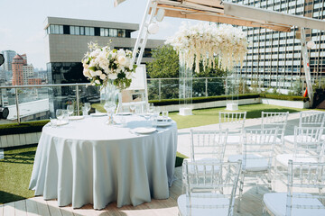 Wedding table setting decorated with fresh flowers in a brass vase. Wedding floristry. Banquet table for guests outdoors with a view of green nature. Bouquet with roses, eustoma and eucalyptus leaves.