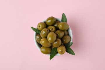 Bowl of olives and leaves on pink background