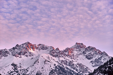 Colors of the passing day; the last rays of the sun on the rocks of the mountain peaks on the background of sky with clouds at sunset  in the winter season