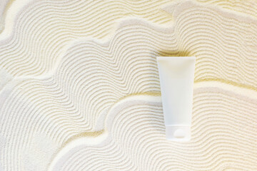 white cosmetic tube on a sand textured background. Copy space