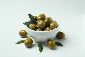 Bowl of green olives and leaves on white background