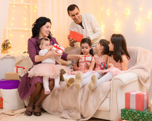 family portrait of a parents and children, sitting on a couch in home interior decorated with lights and gifts