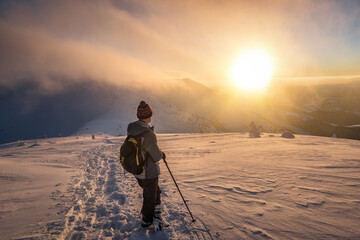 hiker with backpack lookin at sunset in winter mountains