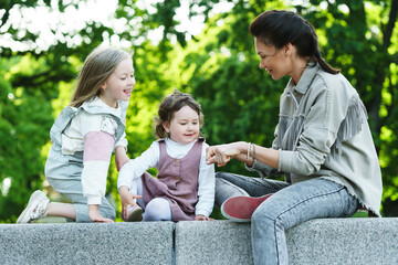 Happy mother and her two daughters sitting and playing in a city park