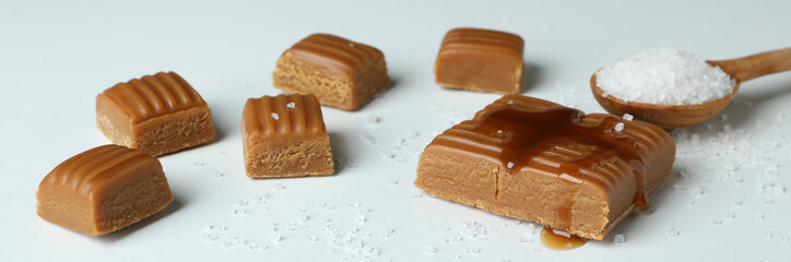 Caramel pieces and spoon of salt on white background