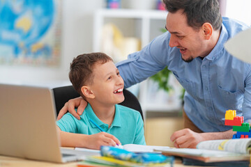 Obraz premium happy father helps his son with his homework using a laptop during distance learning. A parent explains a new topic to a child in an online lesson. Achieving excellence together and enjoying success