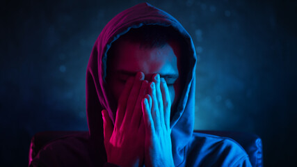 Young male neon portrait cyber style, covers his face with his hands from fatigue, depression and...